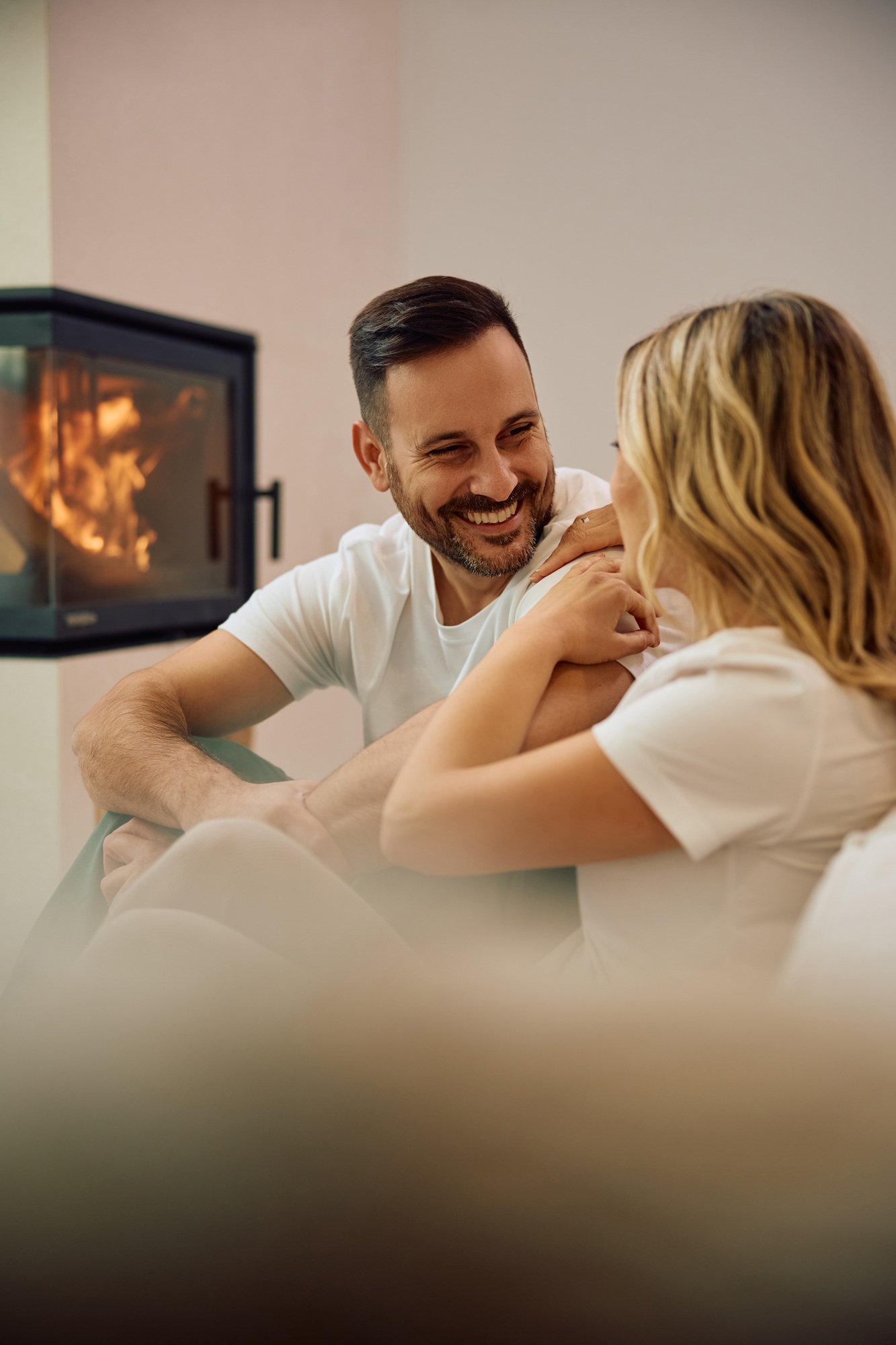 Happy couple talking while relaxing by fireplace at home.