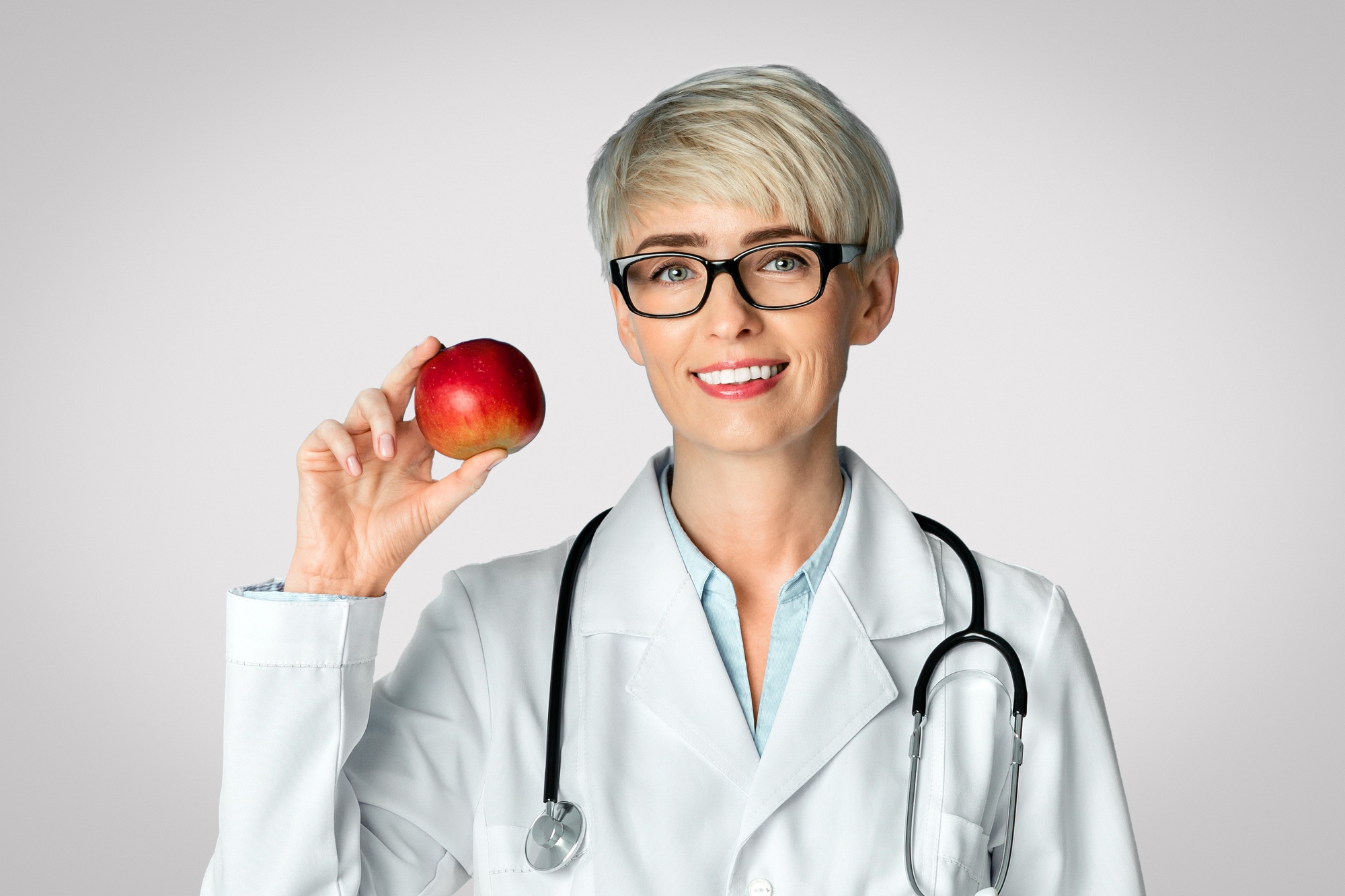 Healthy eating concept. Adult woman doctor in glasses holds red apple in hand